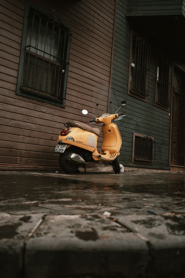 A bright yellow scooter parked beside a wooden building on a rainy urban street.