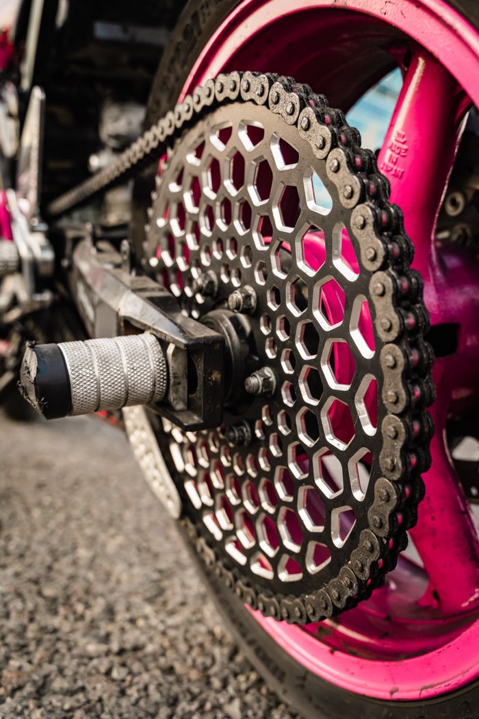 Detailed macro shot of a motorcycle gear wheel with pink accents and chain.