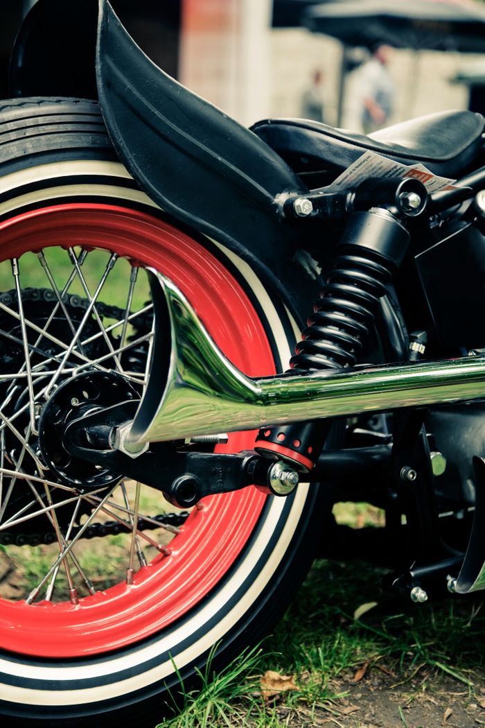 Detailed view of a retro motorcycle with vibrant red wheel rim and chrome exhaust.